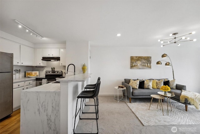 kitchen featuring appliances with stainless steel finishes, white cabinetry, a peninsula, under cabinet range hood, and a kitchen breakfast bar