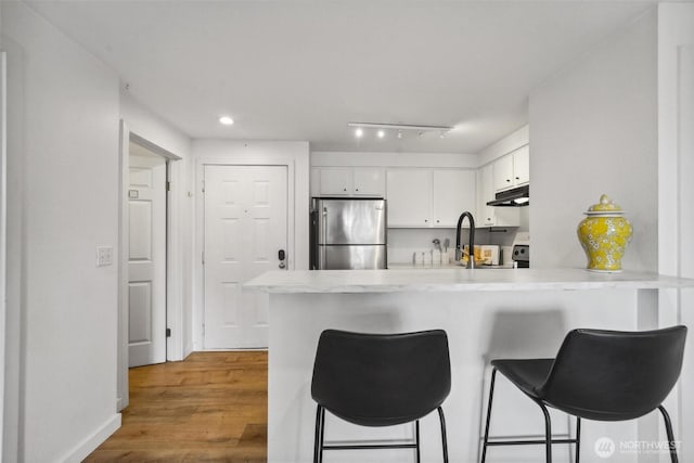 kitchen featuring wood finished floors, freestanding refrigerator, a peninsula, light countertops, and white cabinetry