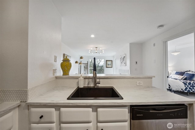 kitchen featuring light stone counters, white cabinets, a sink, and stainless steel dishwasher