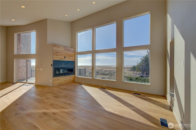 unfurnished living room featuring recessed lighting, a fireplace, visible vents, a towering ceiling, and light wood-style floors