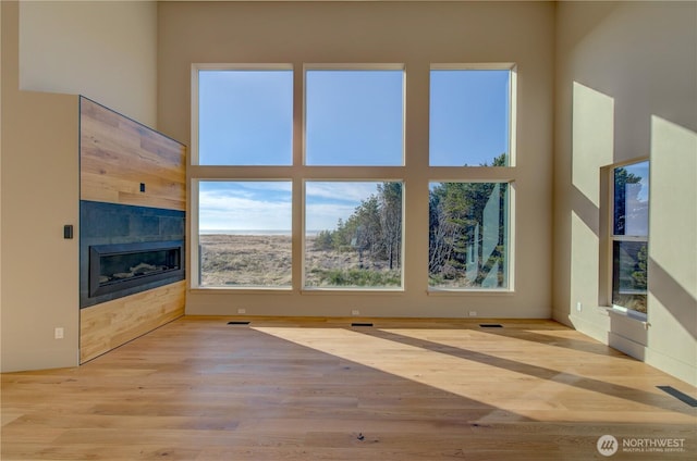 unfurnished living room with a towering ceiling, a tile fireplace, wood finished floors, and visible vents