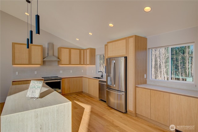 kitchen with wall chimney exhaust hood, appliances with stainless steel finishes, a sink, and light brown cabinetry