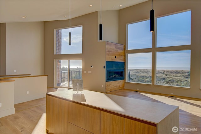 kitchen featuring a tile fireplace, a towering ceiling, light wood-style floors, open floor plan, and modern cabinets