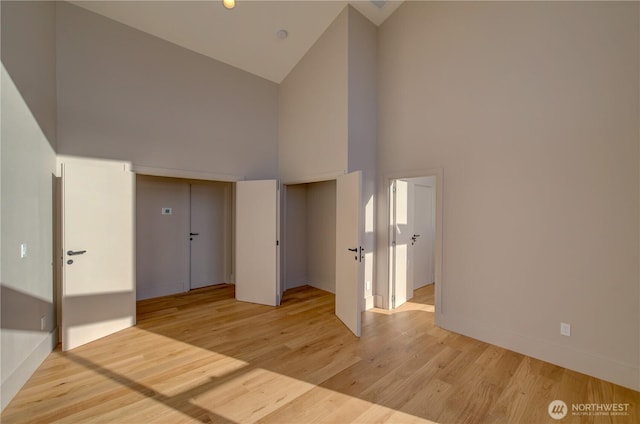 unfurnished room with light wood-style floors, high vaulted ceiling, and baseboards