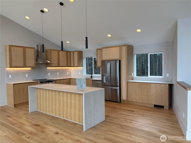 kitchen featuring light wood finished floors, wall chimney exhaust hood, a kitchen island, appliances with stainless steel finishes, and light countertops