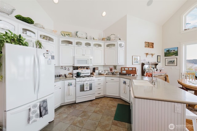 kitchen featuring a peninsula, white appliances, a sink, vaulted ceiling, and light countertops