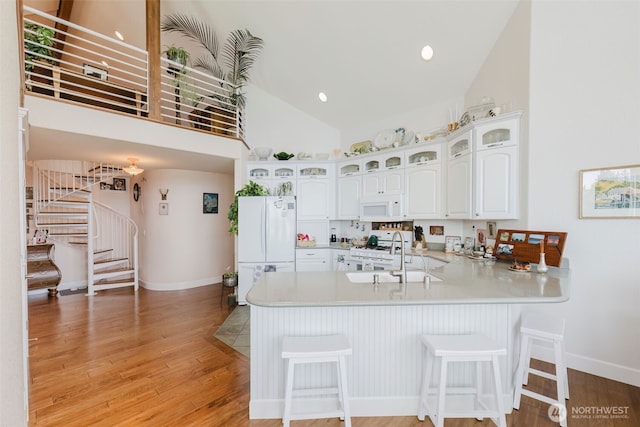 kitchen with a peninsula, white appliances, a sink, light countertops, and light wood-type flooring