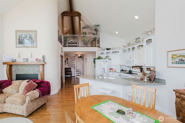 kitchen with white appliances, white cabinets, glass insert cabinets, a peninsula, and light wood-style floors