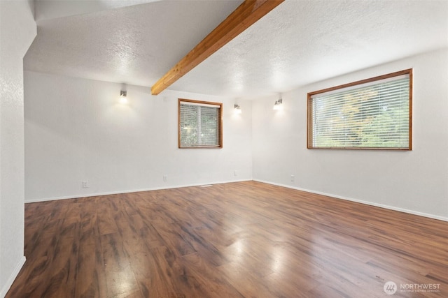 unfurnished room with a textured ceiling, beamed ceiling, wood finished floors, and baseboards