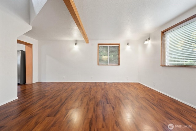 empty room with beam ceiling, a textured ceiling, and wood finished floors