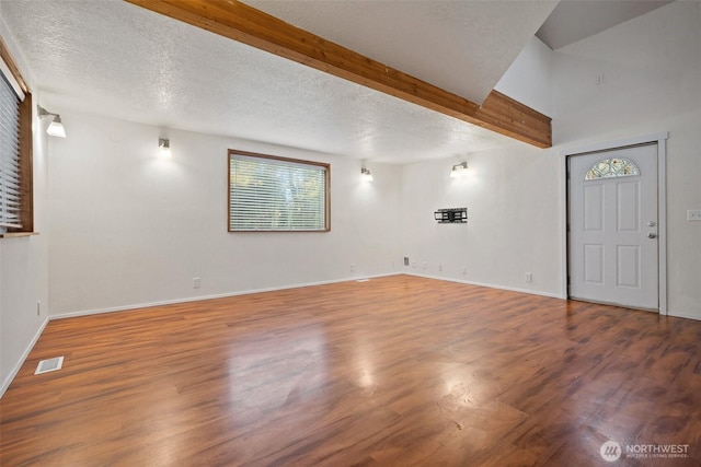 unfurnished living room with a textured ceiling, beam ceiling, wood finished floors, and visible vents