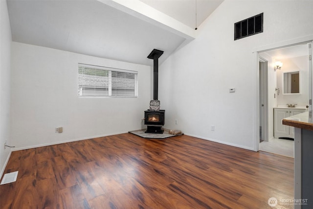 unfurnished living room featuring vaulted ceiling, a wood stove, wood finished floors, and visible vents