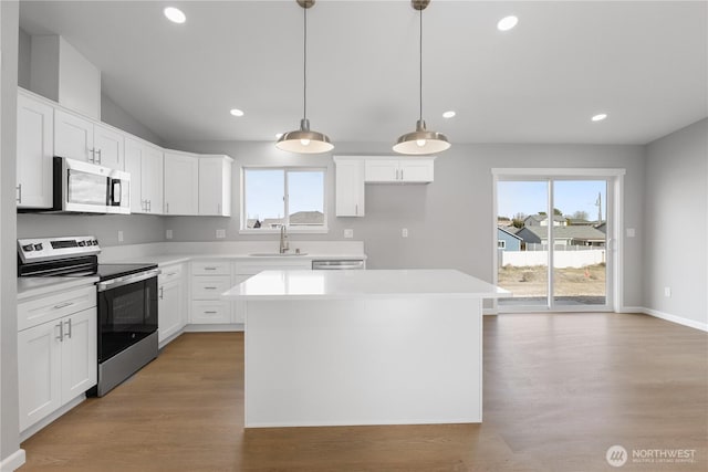 kitchen with light wood finished floors, stainless steel appliances, light countertops, a sink, and a kitchen island