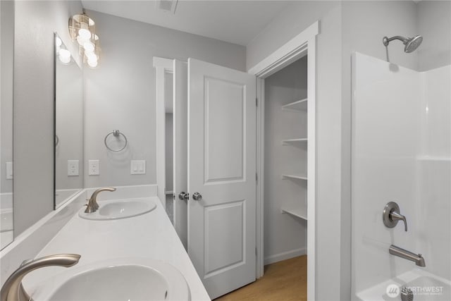 bathroom featuring double vanity, shower / washtub combination, a sink, and wood finished floors