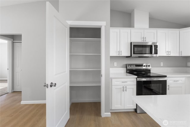 kitchen with white cabinets, appliances with stainless steel finishes, vaulted ceiling, and light countertops