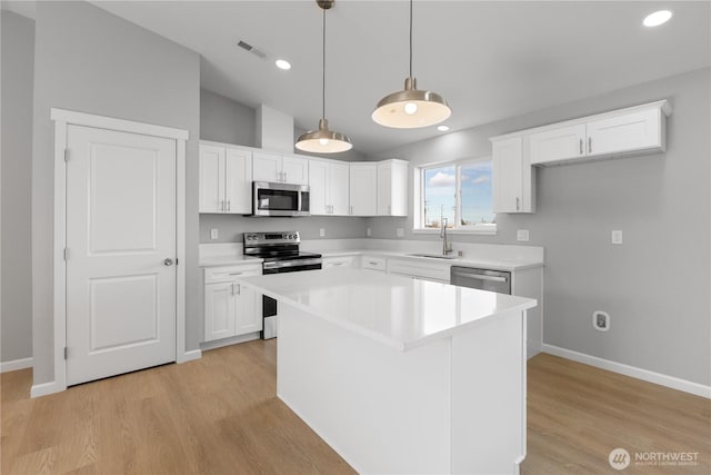 kitchen with light wood-style flooring, stainless steel appliances, a sink, light countertops, and decorative light fixtures