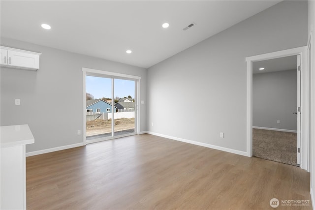 spare room featuring baseboards, visible vents, vaulted ceiling, light wood-style floors, and recessed lighting