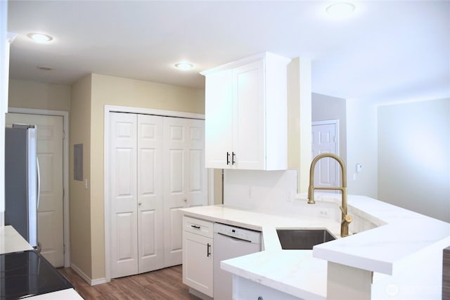 kitchen featuring a peninsula, white dishwasher, freestanding refrigerator, a sink, and white cabinetry