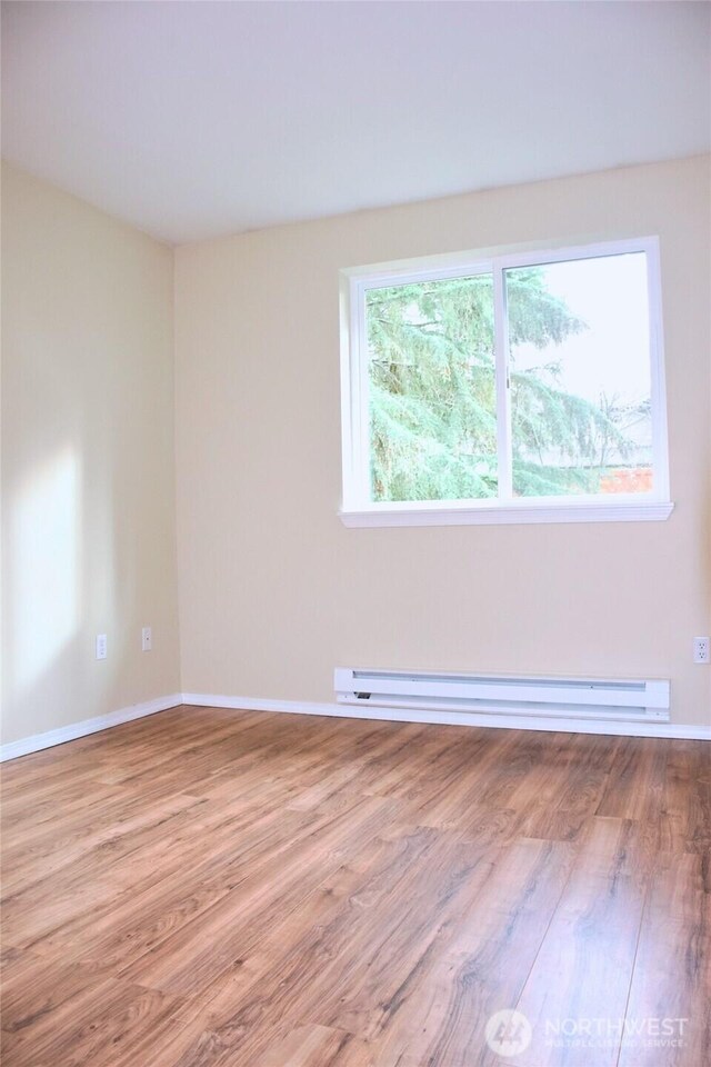 spare room featuring a baseboard heating unit, wood finished floors, and baseboards