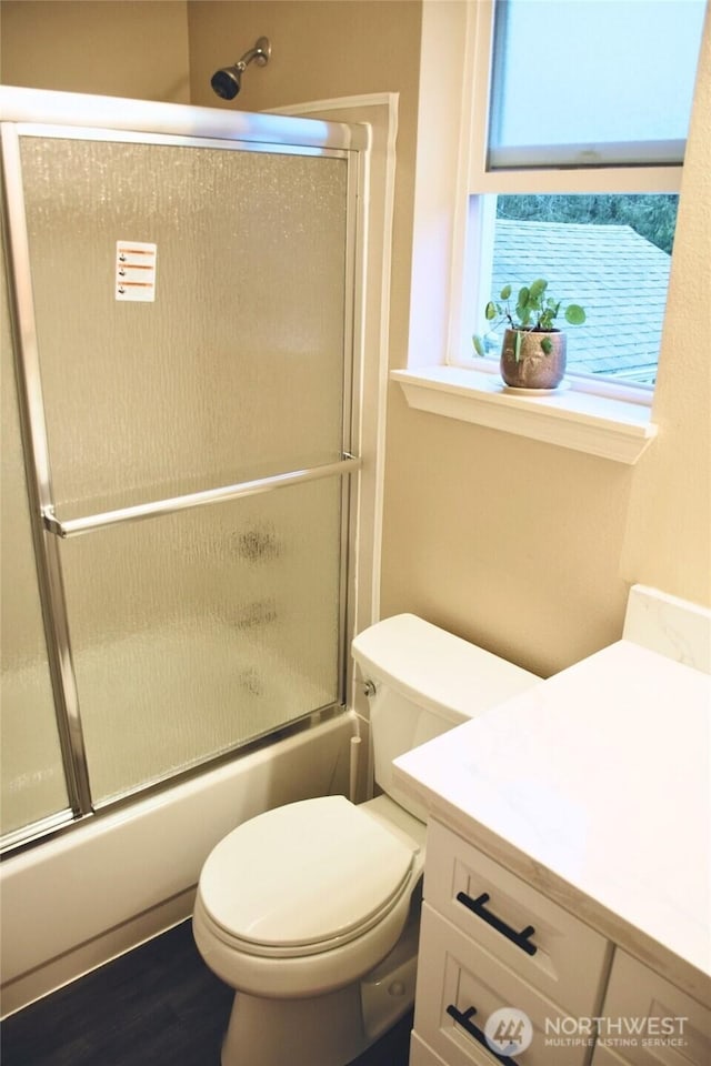 bathroom featuring bath / shower combo with glass door, wood finished floors, vanity, and toilet