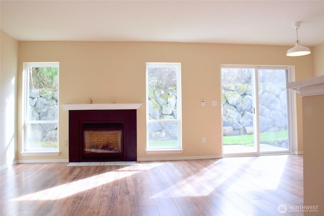 unfurnished living room featuring wood finished floors, a fireplace with flush hearth, and a healthy amount of sunlight