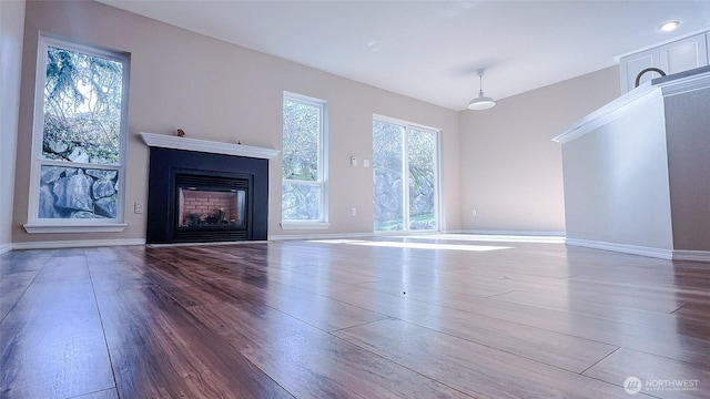 unfurnished living room featuring baseboards, plenty of natural light, wood finished floors, and a fireplace