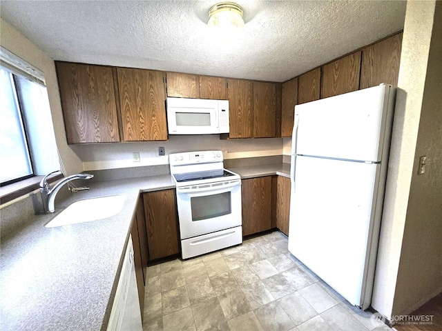 kitchen featuring white appliances, a textured ceiling, light countertops, and a sink