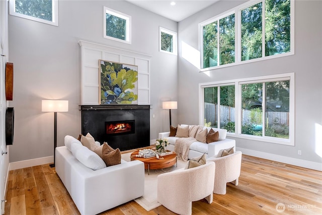 living area featuring a towering ceiling, baseboards, wood finished floors, and a glass covered fireplace