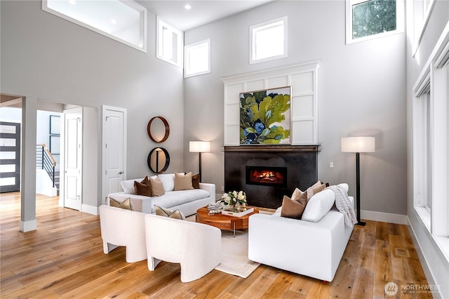 living area with a towering ceiling, baseboards, a lit fireplace, stairway, and light wood finished floors