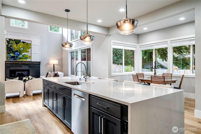 kitchen with stainless steel dishwasher, pendant lighting, light wood-style floors, and a sink