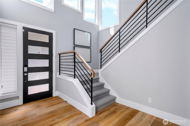 entryway featuring a high ceiling, stairway, hardwood / wood-style flooring, and baseboards