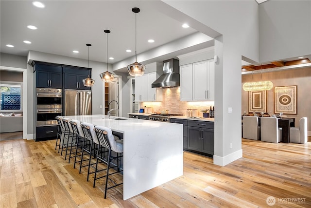 kitchen with a breakfast bar, light wood finished floors, stainless steel appliances, light countertops, and wall chimney range hood