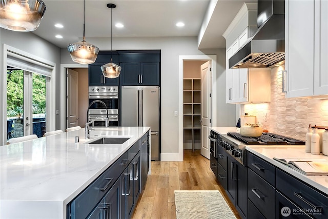 kitchen featuring a sink, white cabinetry, light wood-style floors, wall chimney range hood, and appliances with stainless steel finishes