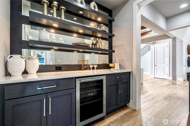 bar featuring beverage cooler, a dry bar, light wood-style flooring, and baseboards