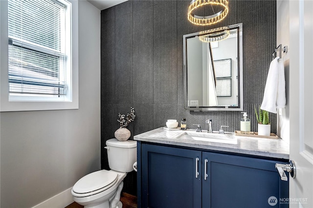 half bathroom with baseboards, vanity, and toilet