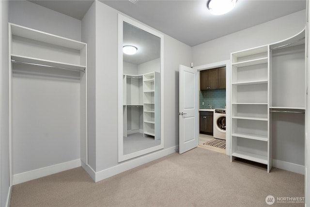 walk in closet with a sink, washer / dryer, and light colored carpet