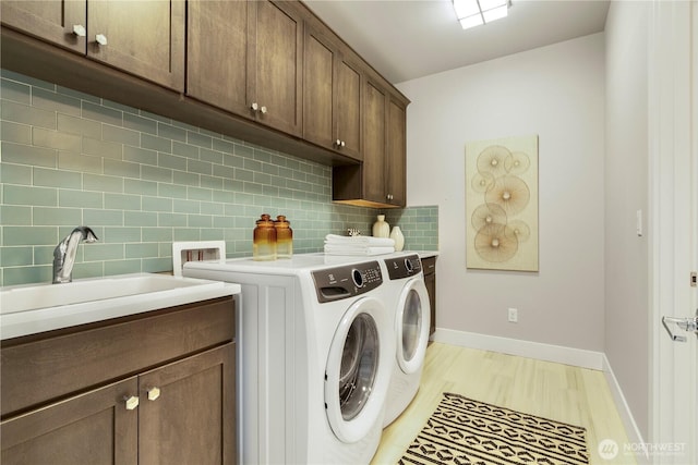 laundry room featuring light wood finished floors, cabinet space, a sink, independent washer and dryer, and baseboards