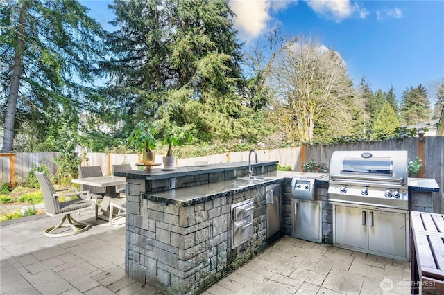 view of patio / terrace with a fenced backyard, a sink, grilling area, and an outdoor kitchen