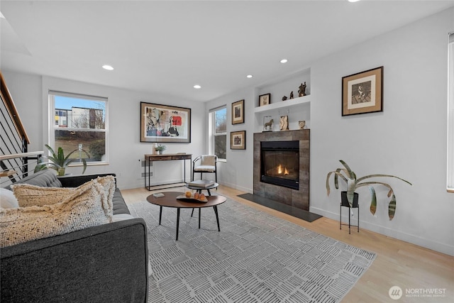 living room with baseboards, built in features, light wood-type flooring, recessed lighting, and a tile fireplace