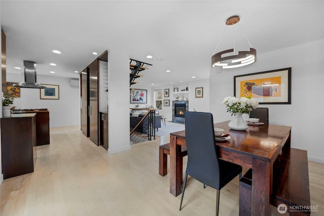 dining area with baseboards, a wall mounted air conditioner, recessed lighting, light wood-style flooring, and a glass covered fireplace