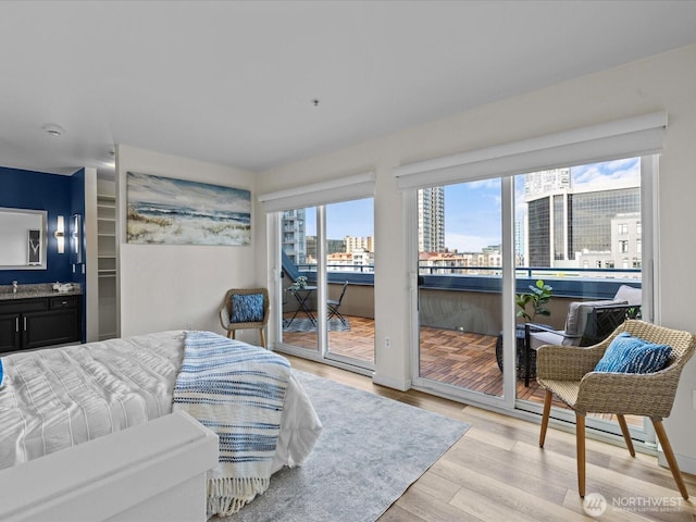 bedroom featuring a view of city, access to outside, ensuite bathroom, and light wood-style floors