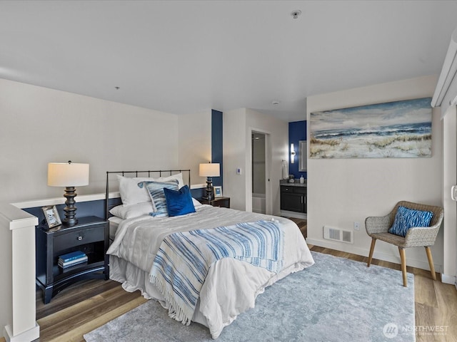 bedroom with visible vents, connected bathroom, baseboards, and wood finished floors