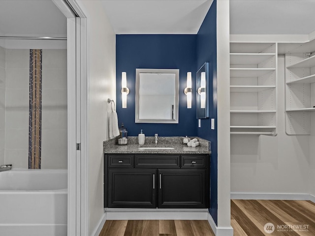 full bath featuring a bathtub, baseboards, wood finished floors, and vanity