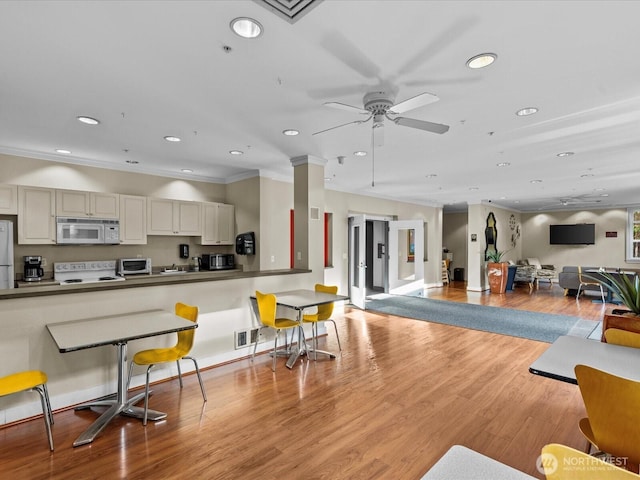 interior space featuring white microwave, light wood-style flooring, stove, dark countertops, and a kitchen bar