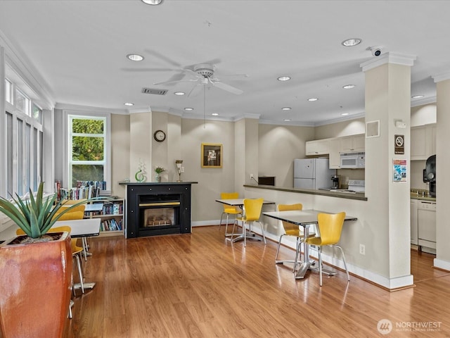 kitchen with ornamental molding, a glass covered fireplace, white appliances, and light wood-style flooring