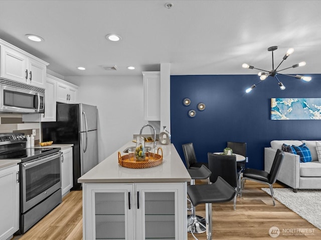 kitchen featuring light wood-style flooring, stainless steel appliances, a sink, white cabinets, and open floor plan