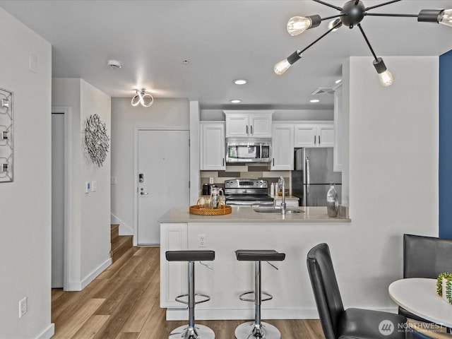 kitchen with a peninsula, white cabinetry, appliances with stainless steel finishes, and wood finished floors