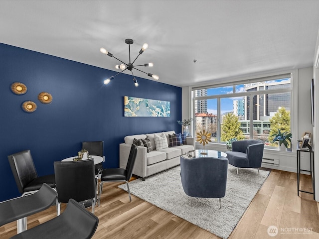 living room featuring a chandelier, an accent wall, baseboard heating, and wood finished floors