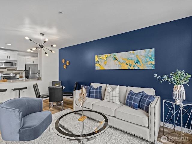 living area with baseboards, an accent wall, a chandelier, and wood finished floors