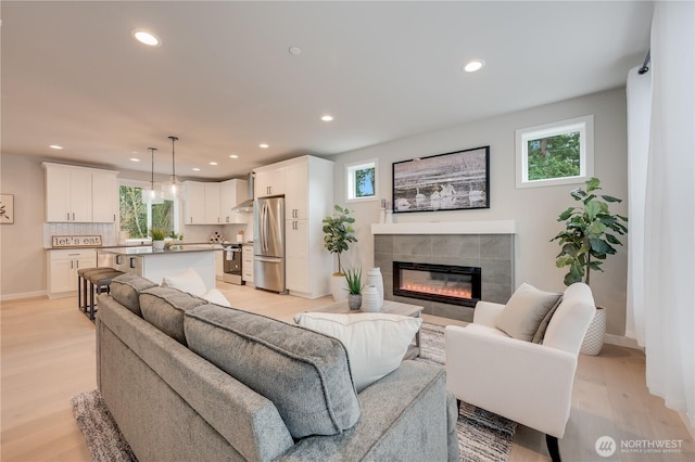 living room featuring a tiled fireplace, plenty of natural light, recessed lighting, and light wood-style floors